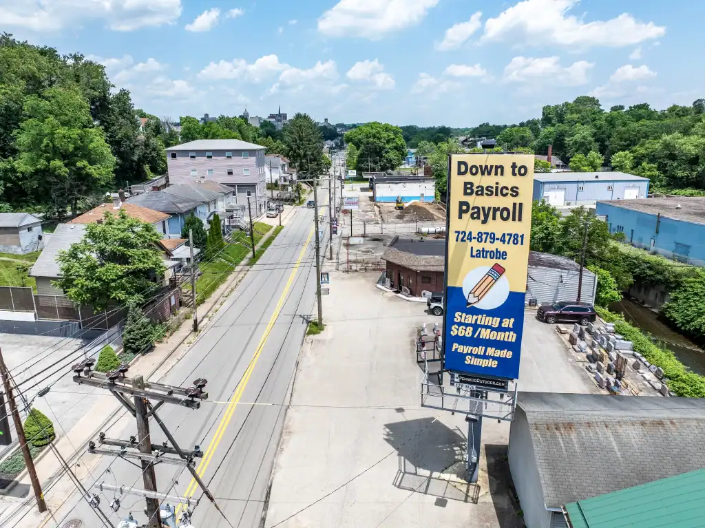 A vertical Penneco Outdoor Advertising billboard featuring a payroll company stands along a road in Greensburg, PA