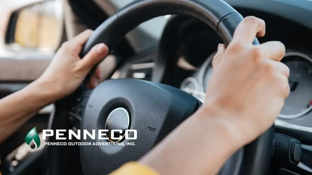 driver with both hands on the steering wheel while passing a digital billboard