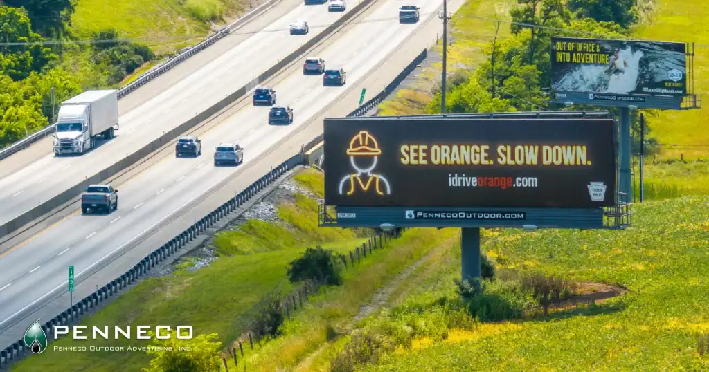 cars and trucks zooming by along the Pennsylvania Turnpike with 2 Penneco Outdoor Advertising billboards perched high above the grass